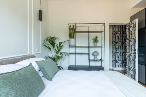 Camera da letto moderna a Roma con cuscini verdi, biancheria bianca, mensole in vetro con piante e decorazioni murali