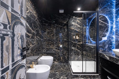 Lussuoso bagno moderno in appartamento romano con marmo nero, sanitari bianchi, cabina doccia in vetro e neon blu