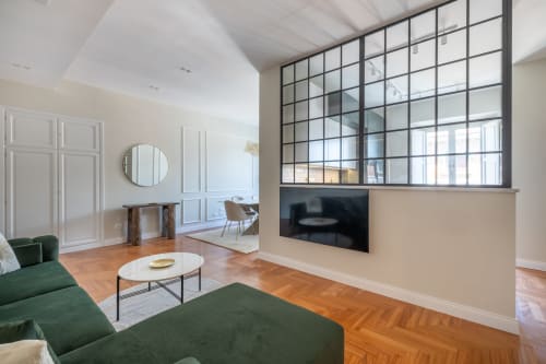 Soggiorno di moderno appartamento romano con divano verde, TV schermo piatto, specchio rotondo e finestra in stile industriale