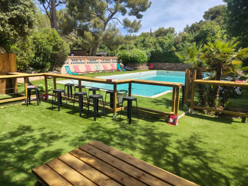 Jardin au bord de la piscine ensoleillé du Camping La Lézardière avec piscine turquoise, chaises longues, table à manger en bois et verdure luxuriante