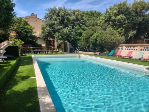 Piscine cristalline du Camping La Lézardière avec transats, jardins luxuriants et bâtiments en brique en Provence