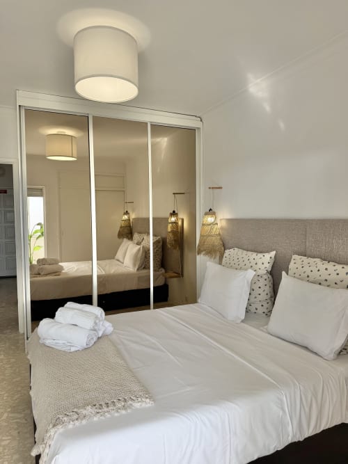 Quarto moderno no apartamento de Aroeira com guarda-roupa espelhado, roupa de cama branca e luminária de teto