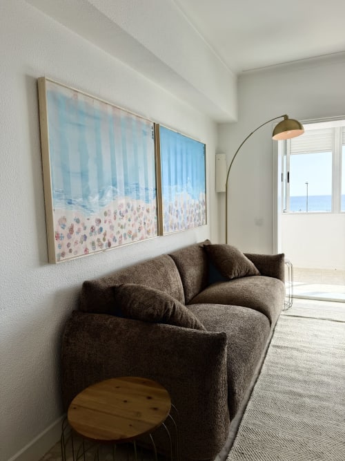 Sala de estar moderna com sofá cinza curvo, mesa lateral de madeira, luminária arco e arte de praia com vista para o mar