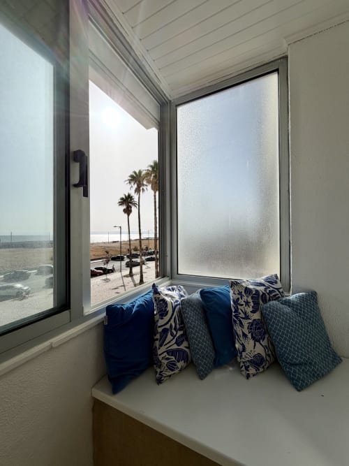 Assento junto à janela com almofadas com vista para a praia e palmeiras no apartamento Republica do Sul, Charneca da Caparica, Portugal