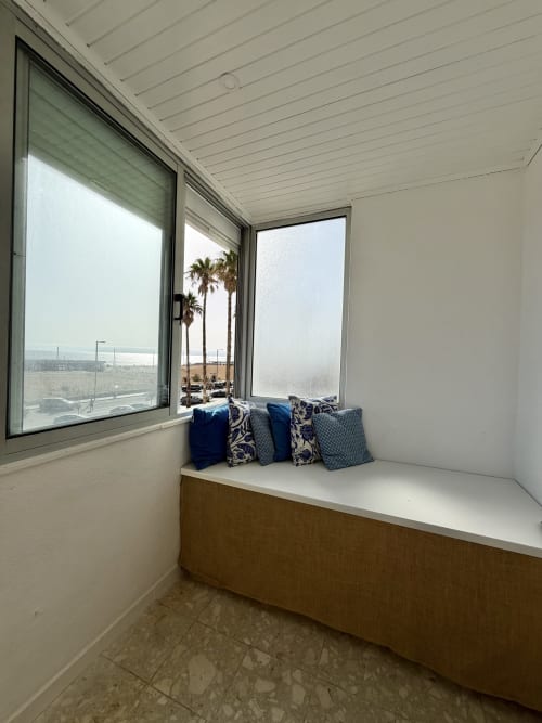 Lugar aconchegante junto à janela com almofadas azuis com vista para palmeiras e praia em República do Sul, Caparica