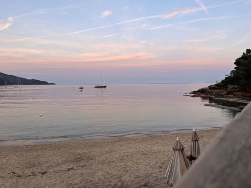 Coucher de soleil tranquille à la plage de l'Hôtel l'Orangeraie Lavandou avec voiliers et parasols fermés