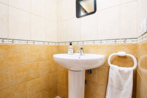 Clean bathroom with pedestal sink, gold tile, white towel rack, and mirror in Casa Reguera villa at FTV Holidays Homes,