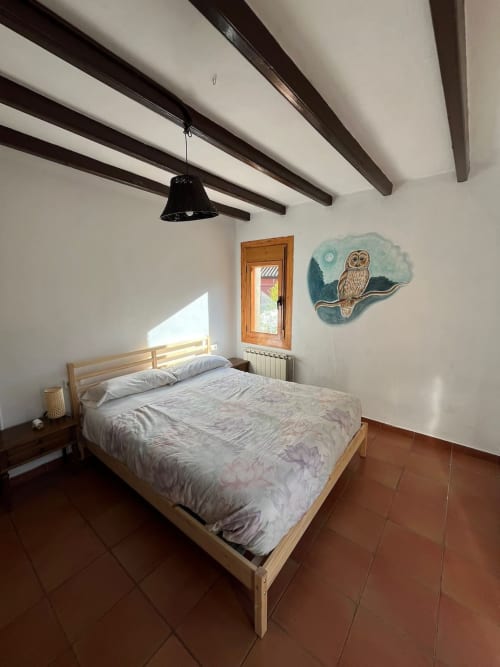 Dormitorio luminoso en la casita L'Amagatall, Vallgorguina, con cama de madera, vigas vistas y decoración con búhos