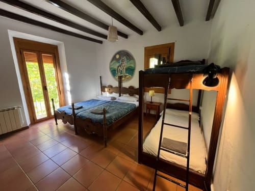 Dormitorio rústico en L'Amagatall de Vallgorguina con vigas de madera, cama doble, litera y vistas a la montaña