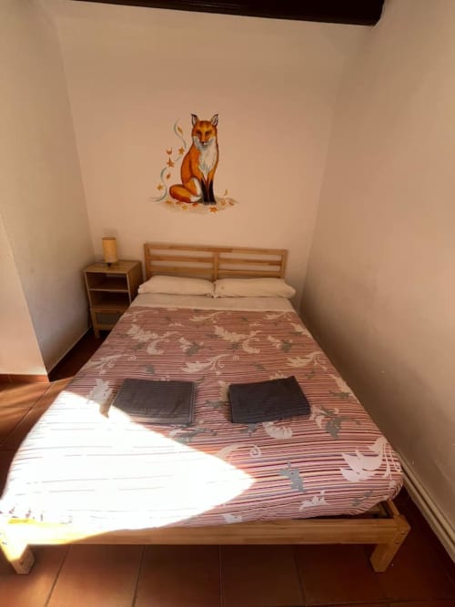 Acogedora habitación en la casita L'Amagatall de Cal Tonedor, Barcelona, con cama de madera, vinilo decorativo de zorro y vistas a la montaña