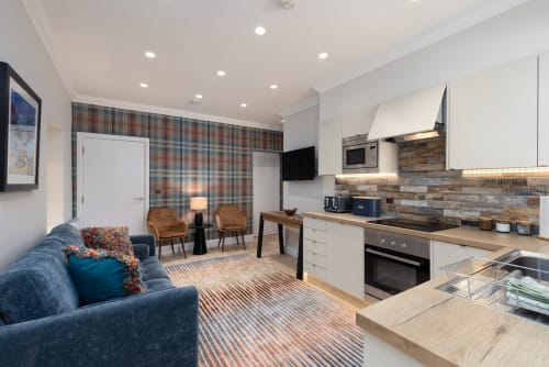 Modern open-plan apartment at The Ford in Perth featuring blue sofa, kitchen with stone backsplash, and tartan accent wall