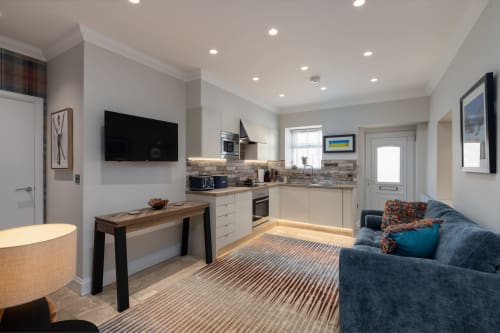 Modern open-plan kitchen and living area at The Ford Apartment, Perth, featuring cream cabinetry, striped rug, blue sofa, and