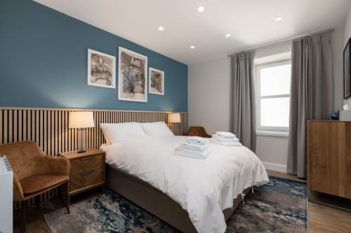 Stylish bedroom at The Ford Apartment, Perth, featuring blue accent wall, wooden bed frame, and modern furnishings