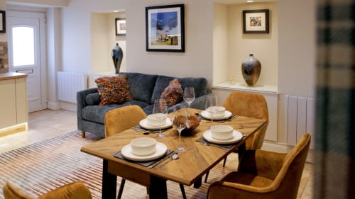 The Ford Apartment dining and lounge area in Perth with wooden table, mustard chairs, grey sofa, and framed artwork.