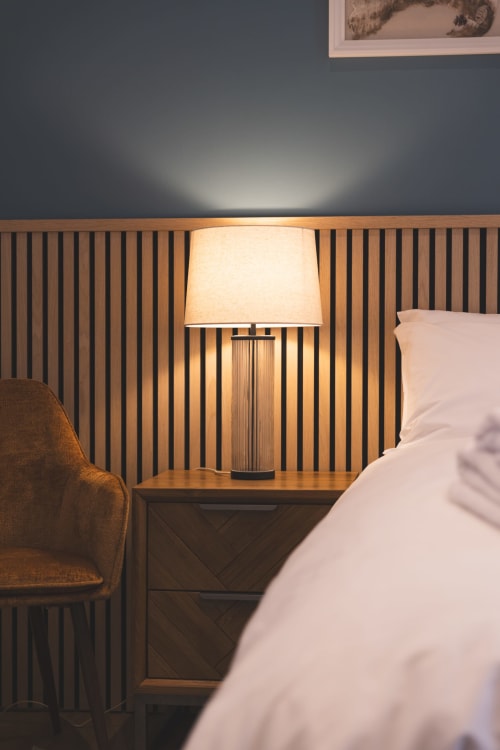 Cozy bedroom corner at The Ford Apartment Perth with bedside lamp, wooden desk, and upholstered chair