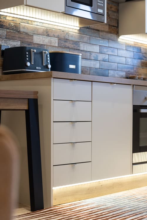 Modern kitchen in The Ford Apartment Perth with white cabinetry, wood countertop, brick backsplash, and under-cabinet