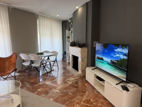 Modern apartment living room in Valencia's Ruzafa Market area with flat-screen TV, dining table, fireplace, and marble