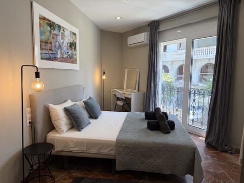 Modern bedroom in The Ruzafa Market Apartment, València, with city views, grey upholstered bed, and balcony doors overlooking