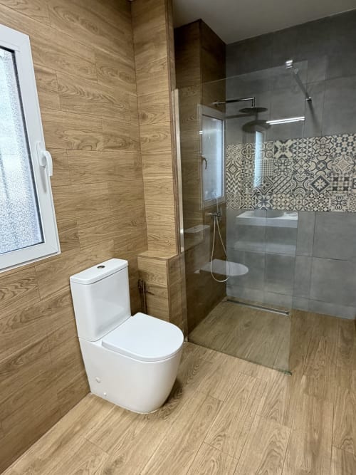 Modern bathroom in The Ruzafa Market Apartment, Valencia with wood-grain tiles, white toilet, walk-in shower with patterned
