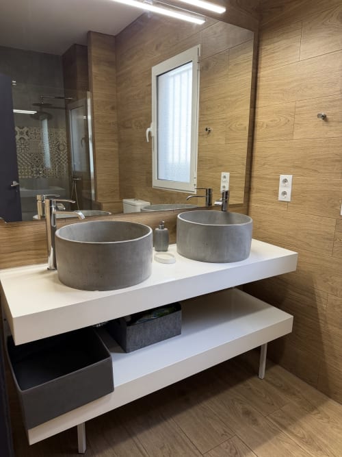 Modern bathroom vanity with two concrete sinks, white countertop, wooden wall tiles, and mirror in Ruzafa apartment, Valencia
