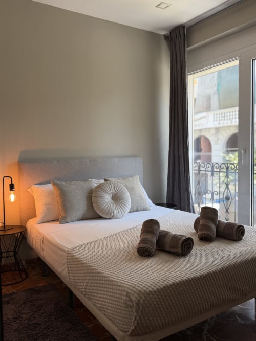 Modern bedroom in Ruzafa Market Apartment, Valencia, with city view balcony, gray headboard, and rolled towels