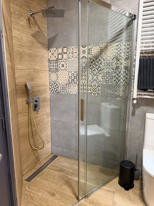 Modern shower enclosure with wood-look tile floor and patterned wall tiles at Stay Gest apartment in Valencia