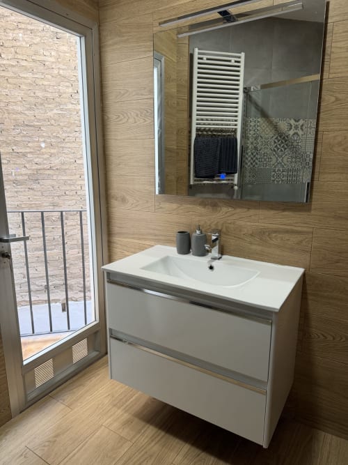 Modern bathroom in The Ruzafa Market Apartment, Valencia, with white vanity sink, mirrored cabinet, and wood-tiled walls