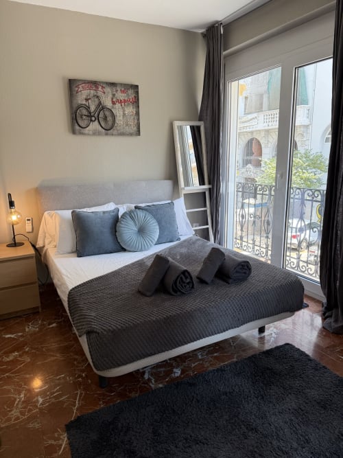 Modern bedroom in Ruzafa Market Apartment, Valencia with city views, gray headboard bed, blue pillows, and Parisian balcony