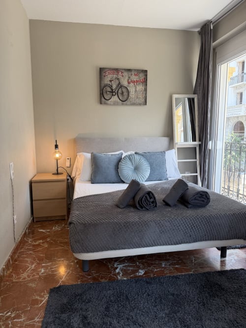 Modern bedroom at Stay Gest apartment in Valencia with city views, bed, nightstand, lamp, and bicycle wall art