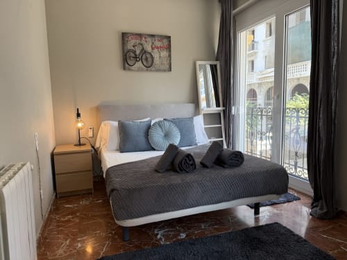 Modern bedroom in Ruzafa Market Apartment, Valencia with city views, gray bed, blue pillows, and balcony overlooking historic