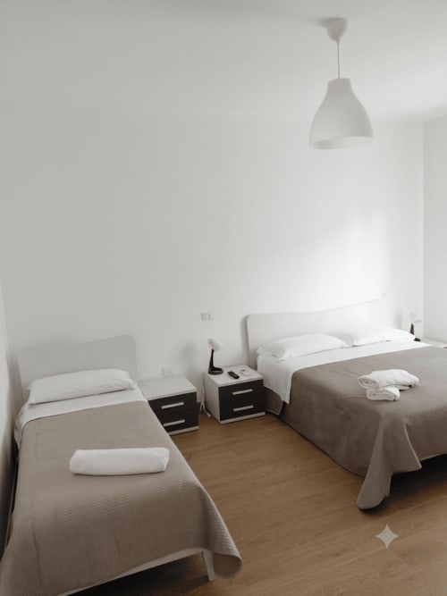 Camera tripla a Makasa B&B a Villapiana con due letti, testiere bianche, lampada sospesa e pavimenti in legno