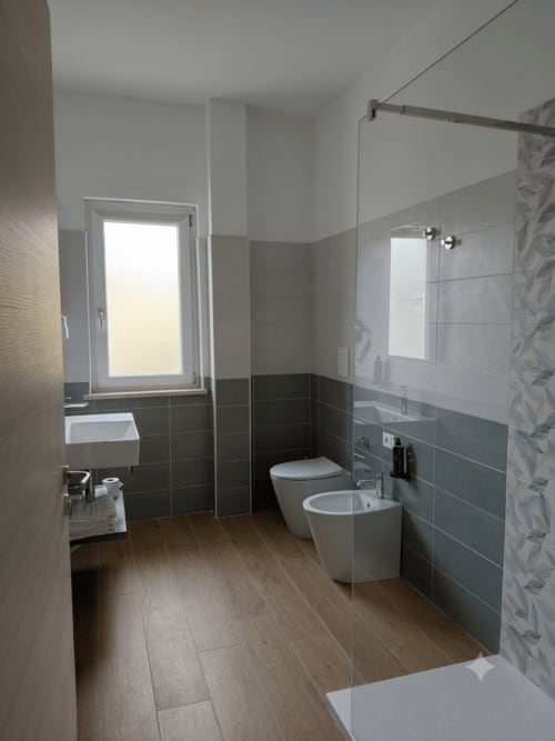 Bagno moderno in Makasa B&B a Villapiana con piastrelle grigie, pavimento in legno, wc, bidet e box doccia in vetro
