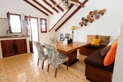 Appartement Anthurium ouvert à Otantik Caribbean avec poutres en bois, table à manger, canapé marron aux accents orange, cuisine