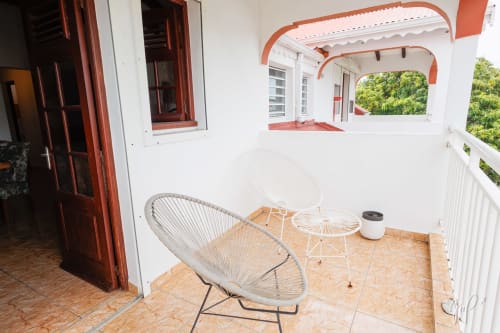 Terrasse couverte avec chaise tissée à l'appartement Otantik Caribbean de Saint-Louis, vue sur la ville visible par les fenêtres