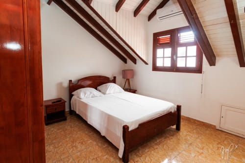 Chambre Anthurium à Otantik Caribbean, Saint Louis - lit en bois avec draps blancs, poutres apparentes, sol en liège et vue sur la ville
