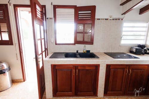 Cuisine moderne dans un appartement caribéen authentique à Saint-Louis, avec armoires en bois foncé, plaque de cuisson noire et fenêtres avec vue