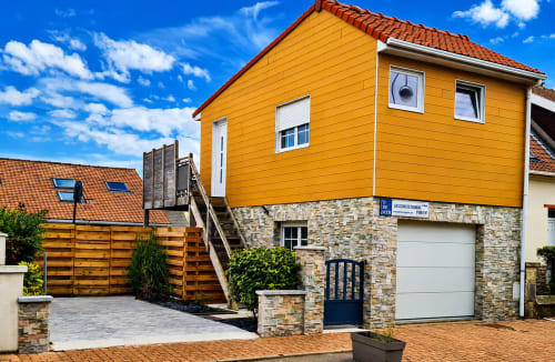 Studio Ô de Mer à Sangatte avec étage supérieur jaune, base en pierre, portails en bois et garage près de la plage.