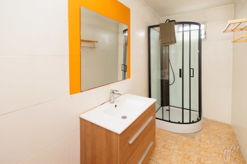 Salle de bain moderne de l'hôtel Otantik Caribbean avec vanité en bois, miroir à cadre orange et douche d'angle noire, Saint Louis