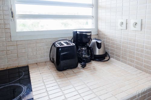 Trois appareils électroménagers sur le plan de travail carrelé de l'appartement caribéen Otantik à Saint-Louis avec fenêtre et prises de courant