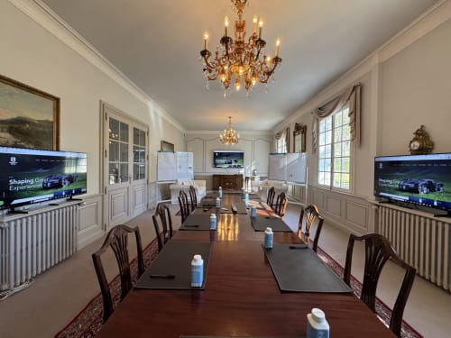 Elegante comedor con larga mesa de madera, candelabro de cristal y televisores de pantalla plana en el manor Domaine de Bize Mirepoix