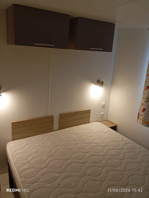 Chambre compacte du mobilhome Le Clocher De Neyran avec lit double, têtes de lit en bois, meubles foncés et murs crème