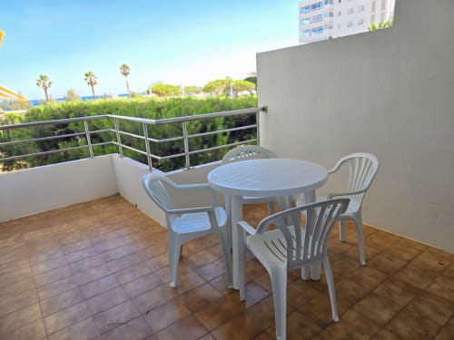 Terrasse d'appartement en bord de mer à Roses avec table à manger, chaises blanches, vue sur la mer et palmiers