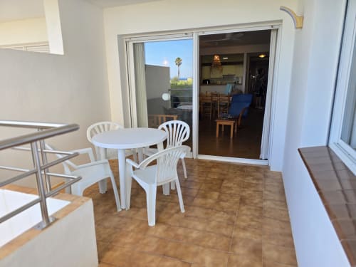 Terrasse d'appartement en bord de mer à Roses avec table à manger blanche, chaises et vue sur la mer par les portes vitrées