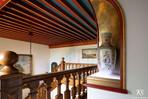 Elegante escalera con barandillas de madera y techo ornamentado en el Domaine de Bize de Mirepoix, con jarrón asiático decorativo
