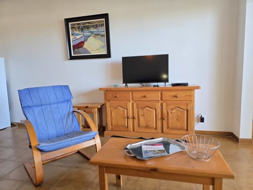 Séjour d'un appartement en bord de mer à Roses avec fauteuil bleu, meubles en bois, téléviseur et tableaux de bateau encadrés