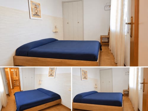 Chambre lumineuse avec lit en bois, literie bleu marine et vue sur la mer dans un appartement à Roses près de la plage