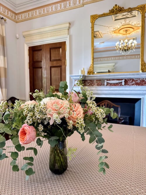 Elegante arreglo floral con rosas rosadas y flores blancas en un jarrón sobre una mesa en una lujosa sala de un castillo francés