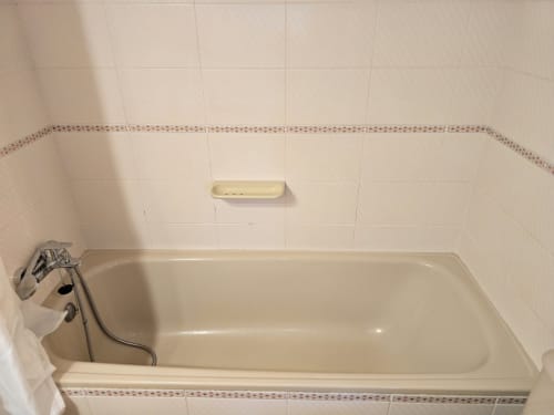 Baignoire beige avec robinetterie chromée dans la salle de bain carrelée de l'appartement à Rosas, Espagne