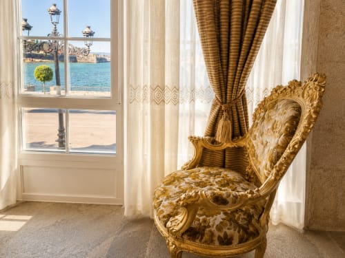 Elegante silla dorada barroca con vistas al mar a través de las ventanas del apartamento frente a playa en Baiona