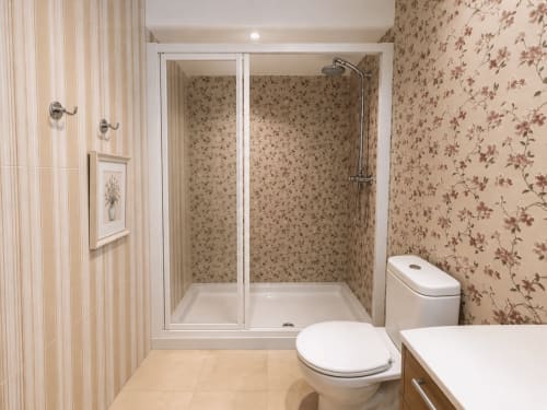 Baño moderno con ducha, inodoro y papel de pared floral en apartamento frente al mar en Holibai, Baiona